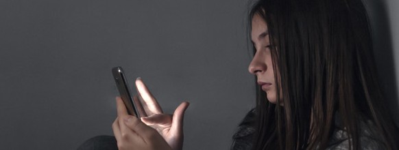 Teen girl excessively sitting at the phone at home. he is a victim of online  social networks. Sad teen checking phone sitting on the floor in the living room at home with a dark background. Victim of online bullying Stalker social networks
